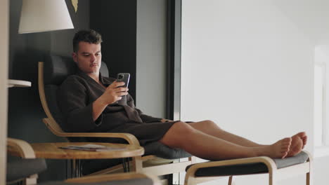 man-is-relaxing-in-lounge-room-of-spa-salon-or-medical-center-after-treatment-surfing-internet-by-smartphone